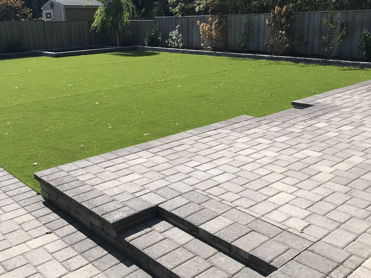 Artificial grass lawn meeting a large paver patio, installed by Oregon Artificial Turf in the Portland area